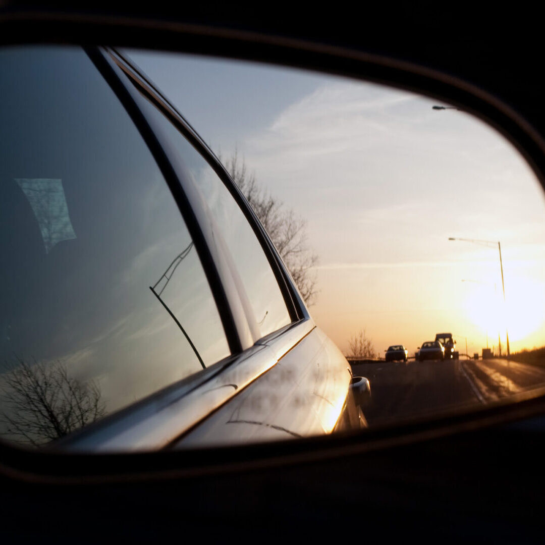 View of the sunset from the side view mirror of a car while driving down the road.  Shallow depth of field. Great image for illustrating blind spots.